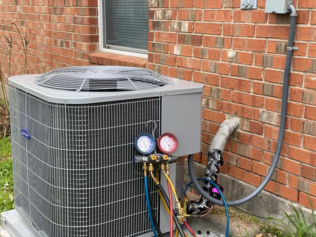 Carrier condenser beside a brick house in Cypress with manifold gauges connected during a charge check
