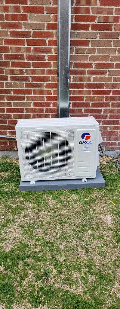 Gree ductless mini split condenser on a pad with the line set chase run up the brick